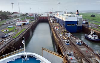 A cruise liner approaching the first of the Panama Canal Locks, Gatun Lock, early in the morning, with the lock gates just opening to allow entry into the first lock. A cargo vessel is in the second parallel lock. Both vessel are heading West towards the Pacific Ocean