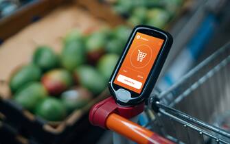 Close up shot of a portable electronic device holding on the shopping cart in supermarket. Smart shopping makes grocery shopping convenient. Contactless payment concept.