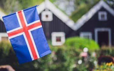 Iceland, Iceland national flag in the foreground, typical icelandic houses with grass on the roof in the background