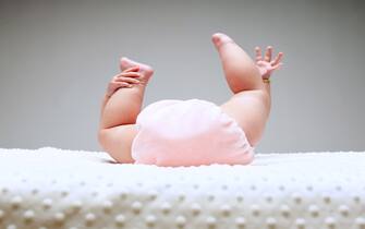 Close-up of a baby lying in bed playing with the toes