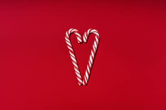 Two candy cane like a heart on red background. Christmas decoration. New Year greeting card. Minimal style. Flat lay