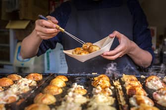 A pari of hands holding chopstick cooking Takoyaki on hot pan. A famous street food in Osaka - Japan.