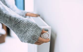 Unrecognizable woman hands in gray sweater touching and setting radiator thermostat regulator