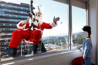 epaselect epa11037148 A man dressed in Santa Claus costume waves to a girl out of the window as he visits Germans Trias Hospital in Badalona, Barcelona, Spain, 19 December 2023. Santa Claus arrived the hospital using a zipline.  EPA/Quique Garcia