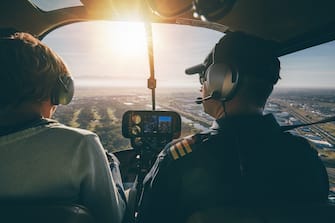 Inside view of a helicopter in flight, with man and woman pilots flying a helicopter on a sunny day.