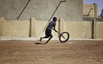 African child playing in the street bare foot with a bicycle wheel.