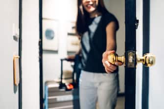 Cheerful young Asian female traveller opening the door entering the hotel room. She is carrying a suitcase and on vacation