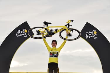 epa10764886 Yellow Jersey and Tour de France overeall winner Danish rider Jonas Vingegaard of team Jumbo-Visma raises his bike as he celebrates on the podium after the 21st and final stage of the Tour de France 2023 over 115kms from Saint-Quentin-en-Yvelines to Paris Champs-Elysee, France, 23 July 2023.  EPA/CHRISTOPHE PETIT TESSON