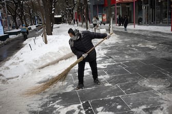epa11030663 A woman brooms snow in a street of Beijing, China, 14 December 2023. Beijing Meteorological Observatory has issued a Cold Wave alert for 15 and 16 December.  EPA/ANDRES MARTINEZ CASARES