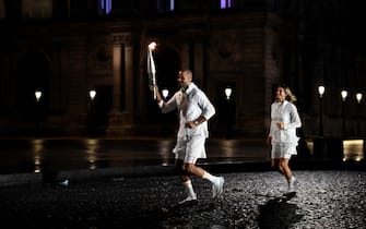 Torchbearer French former basketball player Tony Parker holds the Olympic flame next to French former tennis player Amelie Mauresmo during the opening ceremony of the Paris 2024 Olympic Games in Paris on July 26, 2024, as the Louvre Museum is seen in the background. (Photo by Olivier MORIN / AFP) (Photo by OLIVIER MORIN/AFP via Getty Images)