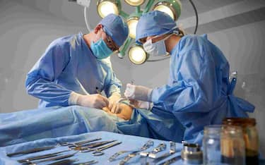 Doctor and assistant performing aesthetic surgery in operating room with various stainless steel tools on blurred foreground. Concept of plastic surgery and medical instruments.