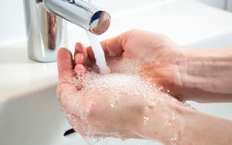 Person is washing her hands under running water from a tap in a bathroom. Symbol image for water wastage.