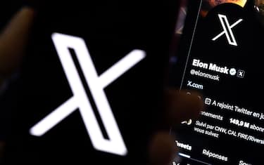 epa10772438 An illustration pictures shows a user holding a mobile phone displaying the 'X' logo in front of Elon Musk's page in Los Angeles, California, USA, 27 July 2023. Twitter announced on 23 July that it will rebrand to X.  EPA/ETIENNE LAURENT