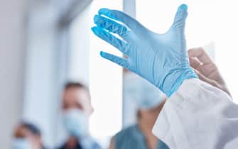 Safety first. Closeup shot of an unrecognizable doctor putting on gloves while treating covid patients in the hospital.