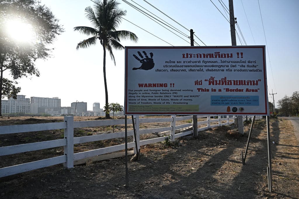 A sign warning of working illegally online is picture in Thailand's Mae Sot district in Tak province near the Myanmar border on February 11, 2025. More than 250 people rescued from online scam centres in Myanmar were handed over to Thailand on February 12, a senior Thai army official said, following a series of crackdowns on the illegal operations. Shwe Kokko, one of the most notorious scam compounds on the Myanmar side, is a built-up city, and security has been tightened in the area, with several Thai military checkpoints and signs warning of Thais and foreigners being "deceived" into working illegally online. (Photo by Lillian SUWANRUMPHA / AFP) (Photo by LILLIAN SUWANRUMPHA/AFP via Getty Images)          