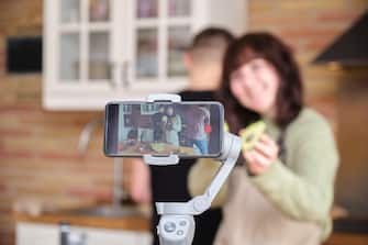 Young woman showing an avocado to the camera and recording a video with her smartphone for her cooking channel. Content creator and influencer.