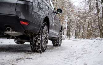 Close-up of winter car tires in a winter scenario with snow and trees in a mountain road