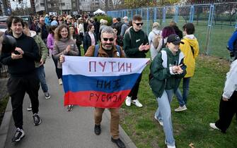 Voters applaud as Peter Nikitin (C), a Russian pro-democracy activist, holds a Russian flag with writting reading "Putin is not Russia" outside a polling station set up in a Russian Embassy School on the day of Russia's presidential election, in Belgrade, on March 17, 2024. (Photo by OLIVER BUNIC / AFP)