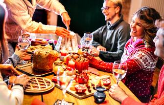 Happy young friends tasting Christmas sweet food having fun at home supper party - Winter friendship concept with millenial people enjoying new year's eve dinner eating together - Warm filter