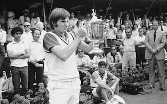 (Original Caption) NEW YORK: As men's singles victor Jimmy Connors holds up the trophy, Ken Rosewall, whom he defeated, looks on at lower right at the U.S. Open tennis tourney at New York's Forest Hills September 9. Connors won 6-1, 6-0, 6-1.