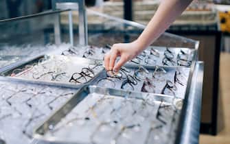 Cropped shot of young Asian woman selecting eye glasses from retail display in optical shop