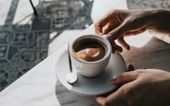 Close up of woman's hand holding a cup of coffee, drinking coffee in outdoor cafe against beautiful sunlight, having a relaxing moment. Enjoying life's simple pleasures