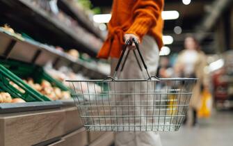 Lower section of young woman standing next to product aisle and choosing vegetables in the store. Young Asian woman doing grocery shopping in supermarket.