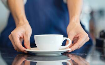 Coffee Shop Franchise and Point of Sale (POS) Solution for Small Businesses. The unrecognizable waitress serving a cup of coffee to a customer at a cafe counter.