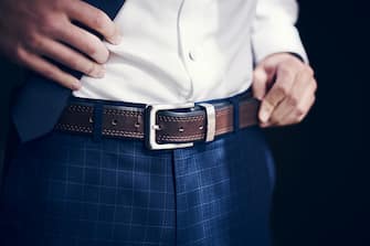Cropped shot of a man wearing a belt with his jeans and shirt on his wedding day