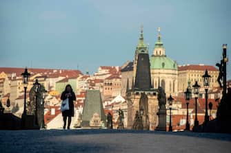 A woman wearing protective mask walks across the empty Charles Bridge on March 16, 2020  in Prague. - The Czech government imposed new restrictions on movement to combat the spread of the coronavirus Sunday, adding to measure that have closed shops, restaurants, pubs and schools and banned gatherings of more than 30 people. (Photo by Michal Cizek / AFP) (Photo by MICHAL CIZEK/AFP via Getty Images)