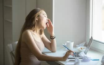 Profile portrait of attractive woman yawning at the laptop
