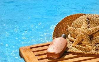 Suntan lotion and straw hat by the pool