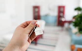 Mortgage concept. Men hand holding key with house keychain. Modern light lobby interior. Real estate, moving home or renting property.