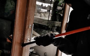 Burglar with crowbar trying break the door to enter the house