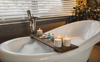 Bathroom, decorated for romantic evening. Cozy and quiet atmosphere at home. Pleasure and relaxation in bathroom, female wellbeing. Beautiful candlelight.  Resting in beauty spa. Background with room for copy space.