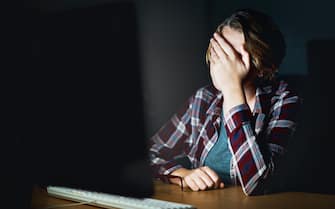 A young woman, busy with her computer at night, puts her hand over her eyes, tired or frustrated.