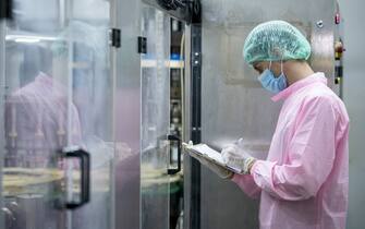 Worker examining a basil seed drink fruit flavors bottles on automated conveyor belt in factory. Food and beverage industry business.