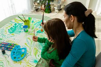 Caring and creative Caucasian mother and daughter, together paint plants on the paper with watercolors