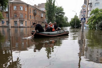 Volunteers carry local residents on an inflatable boat during an evacuation from a flooded area in Kherson on June 8, 2023, following damages sustained at Kakhovka hydroelectric power plant dam. Ukrainian President Volodymyr Zelensky visited the region flooded by the breached Kakhovka dam on June 8, 2023, as the regional governor said 600 square kilometres were underwater. (Photo by ALEKSEY FILIPPOV / AFP)