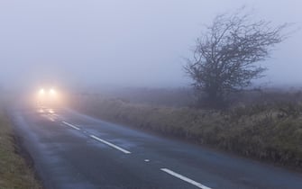 A car approaches in dense fog on uk road on Exmoor national park.  The low visibility makes for dangerous driving conditions.