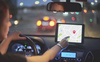 Rear view of woman driving car and touching screen of navigation system