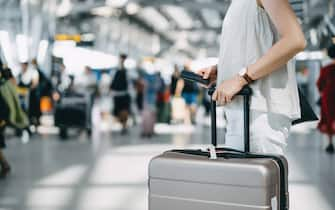 Cropped image of young woman holding passport and suitcase walking in the international airport hall