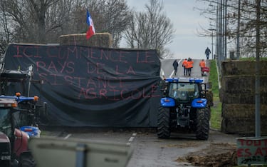 People walk near tractors with a banner reading "Here begins the country of agricultural resistance" blocking an access road to the Golfech nuclear power station, during a protest by farmers over a number circumstances affecting their sector, in Golfech, southern France, on January 22, 2024. . France's powerful farming union on January 22 threatened a week or more of protest action as it was poised to meet with the prime minister. The unions have demanded concrete government action to address their grievances, which they say include excessive financial charges and environmental protection rules. (Photo by Ed JONES / AFP)