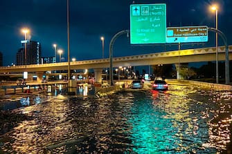 TOPSHOT - Motorisits drive along a flooded street following heavy rains in Dubai early on April 17, 2024. Dubai, the Middle East's financial centre, has been paralysed by the torrential rain that caused floods across the UAE and Bahrain and left 18 dead in Oman on April 14 and 15. (Photo by Giuseppe CACACE / AFP) (Photo by GIUSEPPE CACACE/AFP via Getty Images)