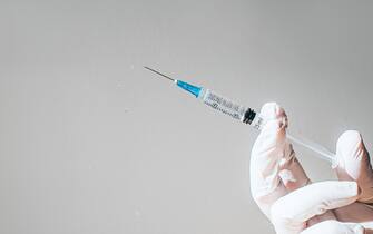 Conceptual image of a gloved hand holding a syringe. Space for copy.