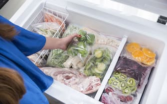 A woman putting green bell peppers into fridge.