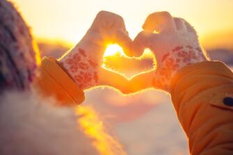 Woman hands in winter gloves Heart symbol shaped Lifestyle and Feelings concept with sunset light nature on background