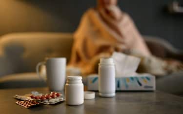 Sick aged woman feeling unwell wrapped in warm quilt. Focus on pills for medical treatment on table
