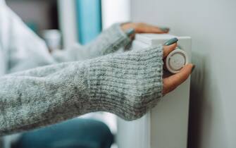 Cropped female hands in warm sweater trying to keep warm near battery radiator. Cold temperature