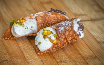 An Italian cannoli filled with ricotta cream on wooden board.